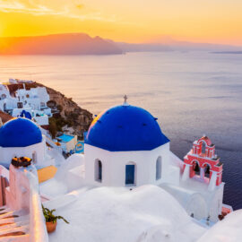 Iglesia de cúpula azul en Oia Santorini con vistas al mar Egeo durante el atardecer.