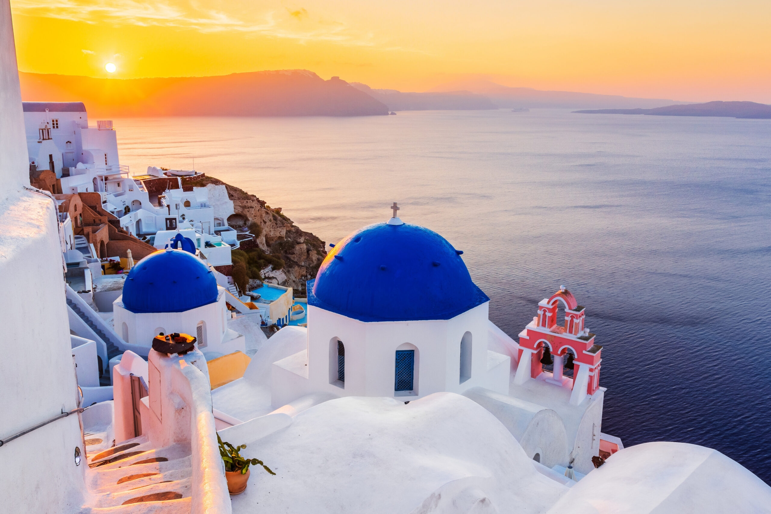 Iglesia de cúpula azul en Oia Santorini con vistas al mar Egeo durante el atardecer.