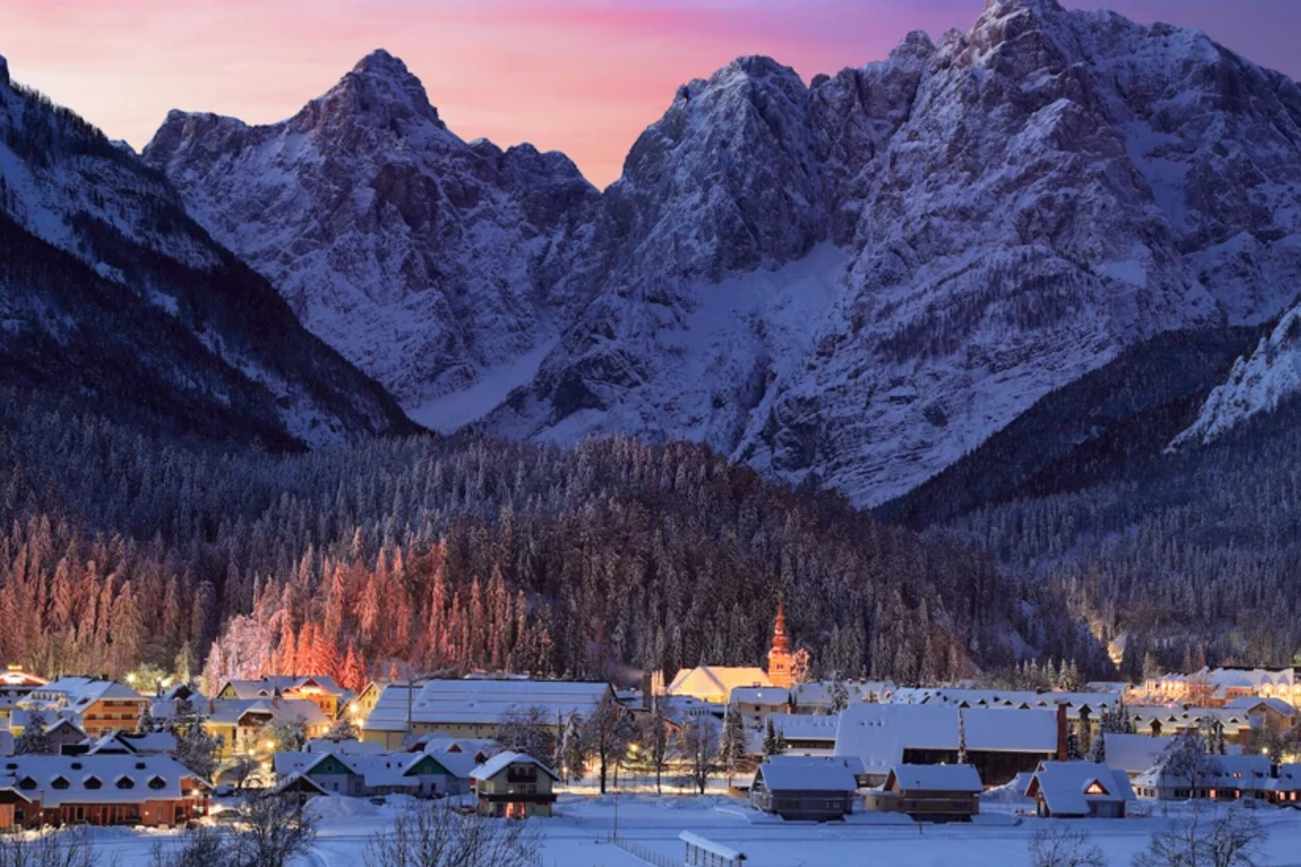 Eslovenia en 10 días - Liubliana Pueblo nevado de Kranjska Gora iluminado al anochecer bajo montañas.